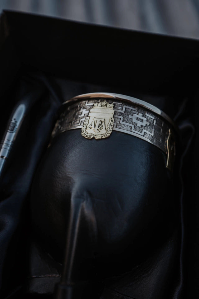 A silver-colored metal mate with black leather detailing, featuring an engraved emblem on the top.